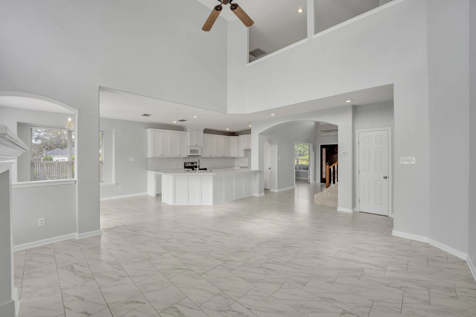 Two-story vaulted ceilings with a ceiling fan, arched doorways, white tile flooring, recessed lighting, and a kitchen with white cabinetry and a subway tile backsplash