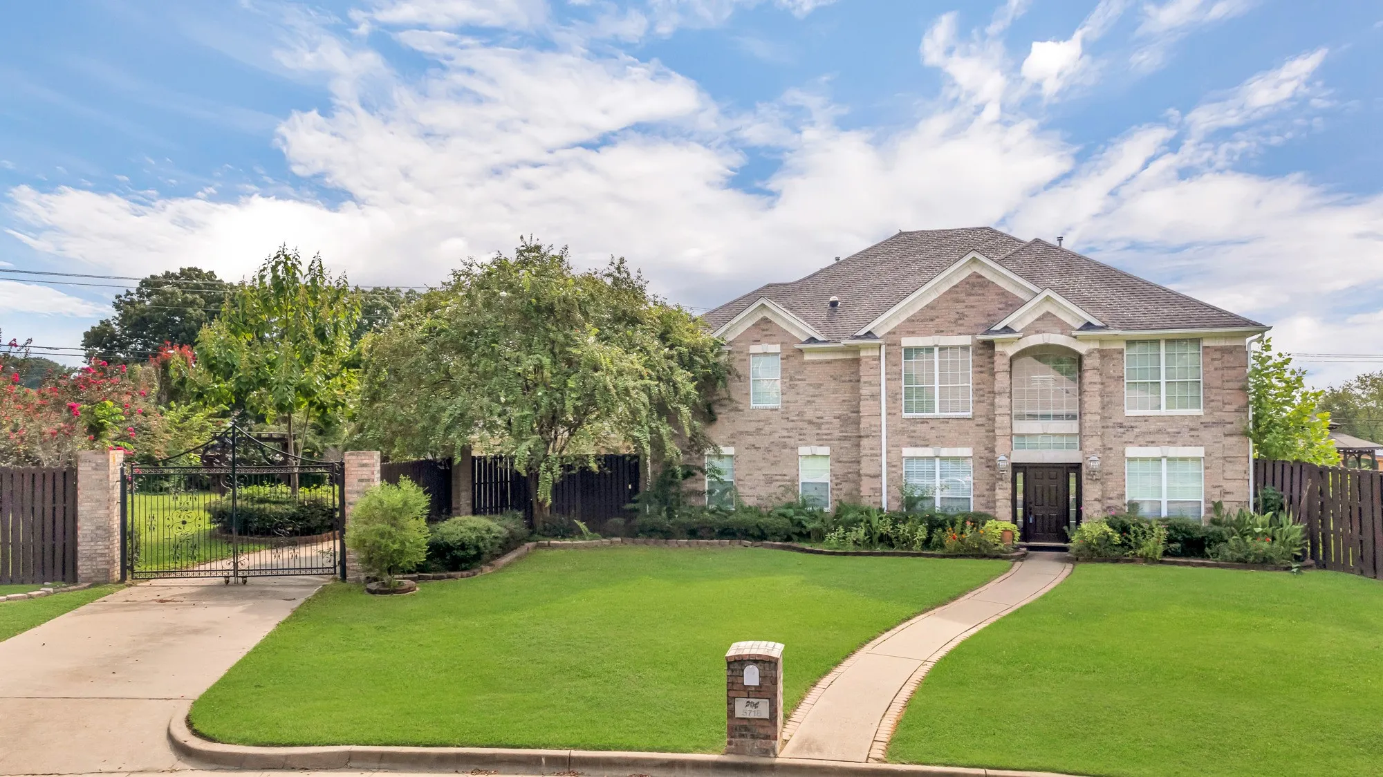 Brick exterior, arched windows, gabled roofline, concrete driveway, and wrought iron gate