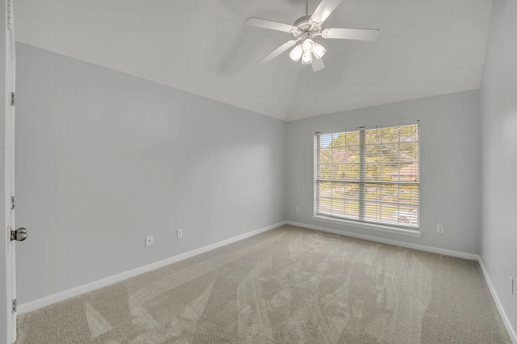 Vaulted ceiling, ceiling fan with light fixture, gray wall paint, window with blinds, and light-toned carpet flooring