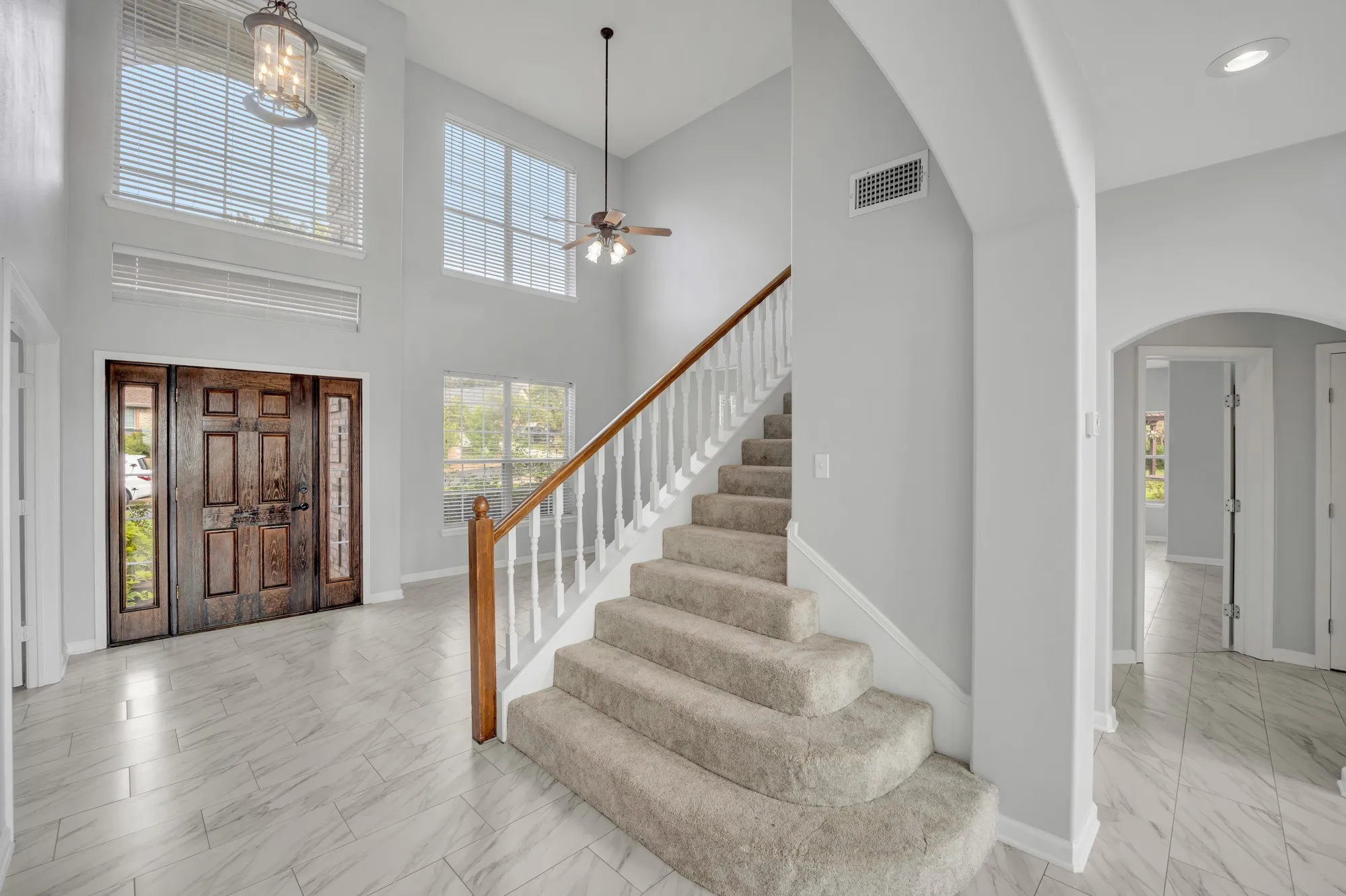Expansive foyer with a two-story ceiling, natural wood double entry doors with integrated sidelights, and light-toned tile flooring