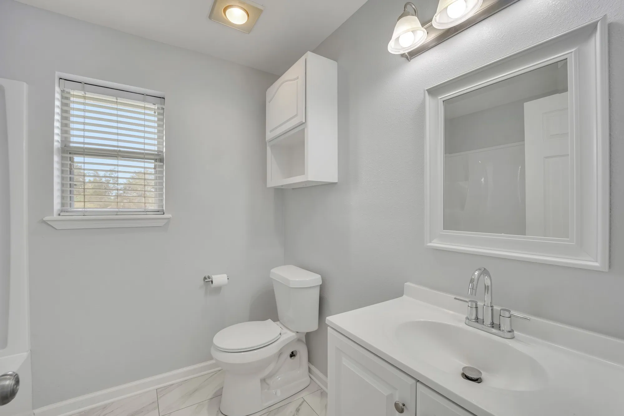 Bathroom featuring a single window, white vanity with integrated sink, chrome faucet, wall-mounted mirror, and white storage cabinetry