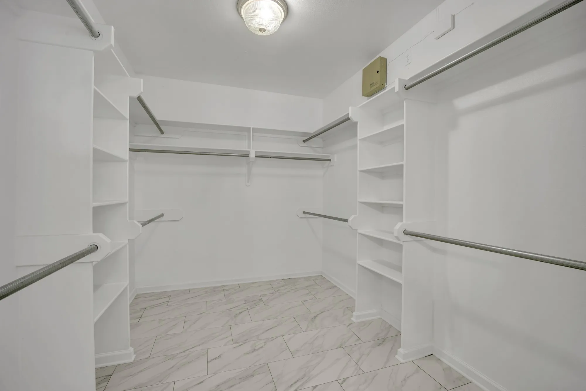 Expansive walk-in closet featuring built-in shelving, multiple hanging rods, and patterned tile flooring