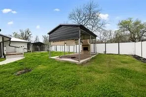 Covered outdoor structure with built-in fireplace, concrete patio, and surrounding grassy area