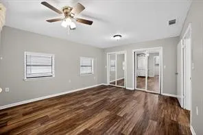 Wood-finish flooring, ceiling fan with light fixture, multiple windows with blinds, and mirrored sliding closet doors