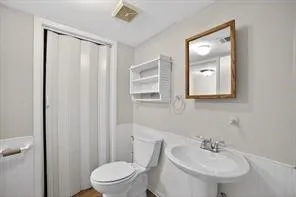 Pedestal sink with chrome faucet, toilet, and a wall-mounted shelving unit