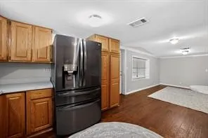 Wood-finish flooring throughout, light wood cabinetry, light countertops, and a modern dark-finish refrigerator