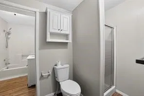 White wall-mounted cabinetry, a toilet, and a glass-enclosed shower