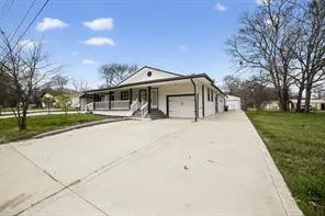 Expansive concrete driveway, attached garage, covered front porch with white railing, and a side-gabled roofline