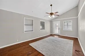 Vaulted ceiling with an attached ceiling fan, rich wood-finish flooring, and a glass-paneled exterior door