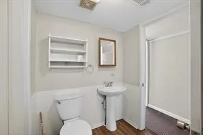 Pedestal sink with chrome faucet, wall-mounted mirror, white toilet, wood-finish flooring, and a shower area with a sliding door