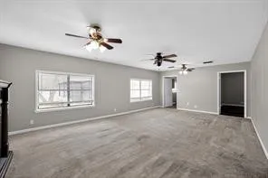 Spacious room with gray wall paint, gray carpet, multiple windows, and ceiling fans