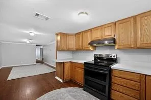 Kitchen featuring wood cabinetry, white countertops, and a black electric range with a coordinating range hood