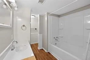 Tub and shower combination with a single-handle faucet, vanity with integrated sink, wood-finish flooring, and wall-mounted medicine cabinet