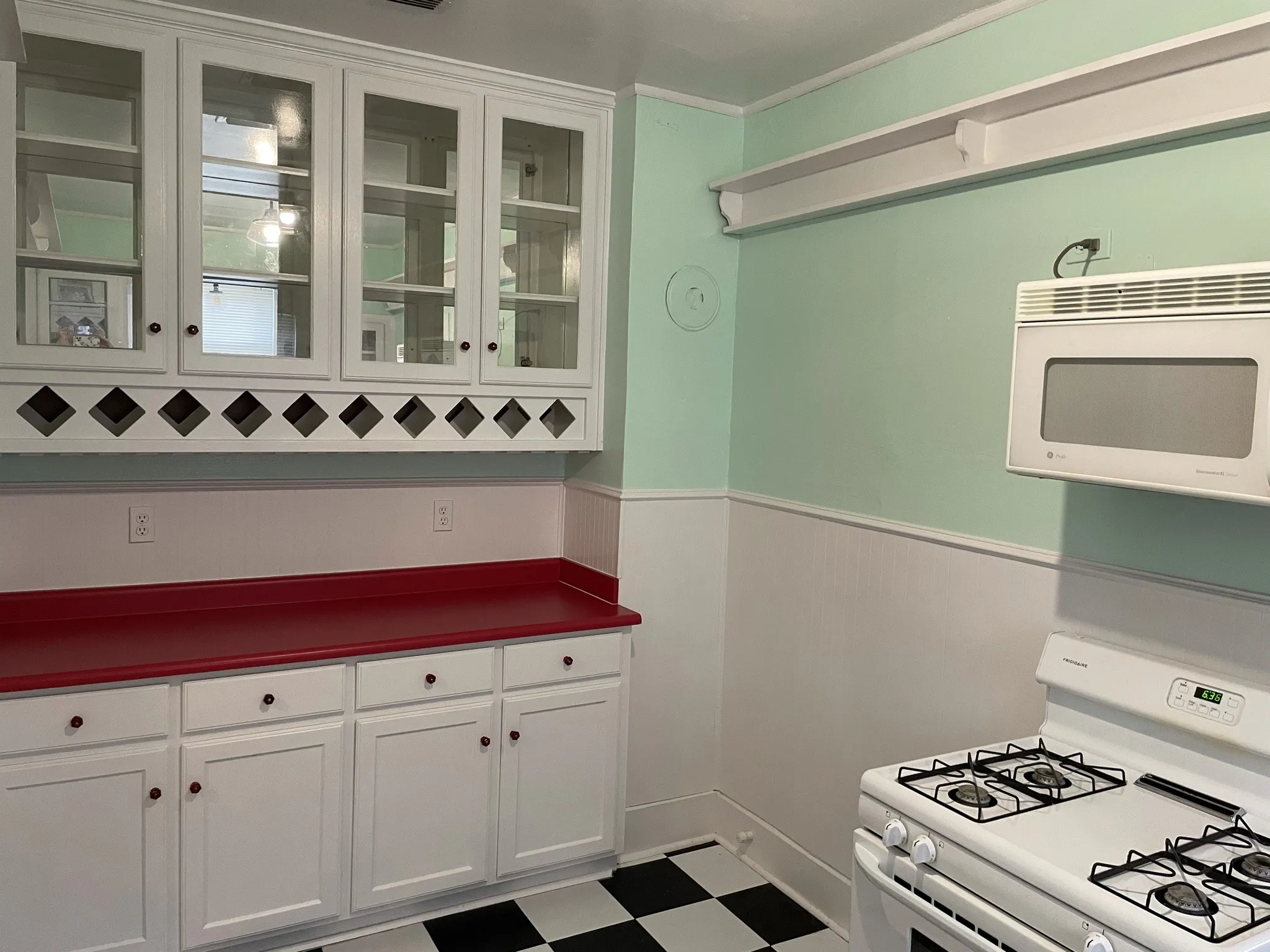 Kitchen featuring white appliances, white cabinets, light flooring, dark countertops, and glass insert cabinets