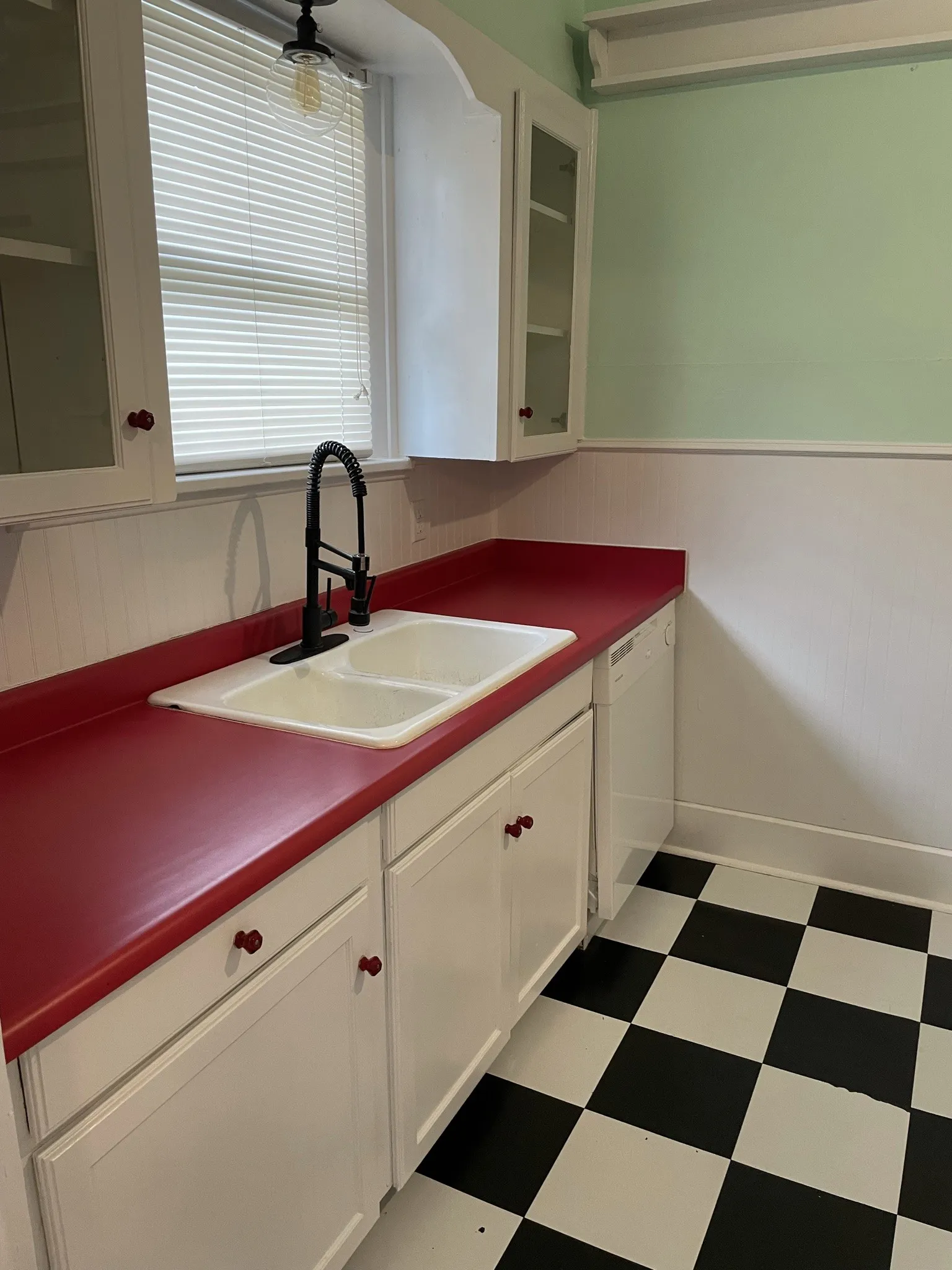 Kitchen with glass insert cabinets, dark countertops, light flooring, white cabinetry, and a wainscoted wall