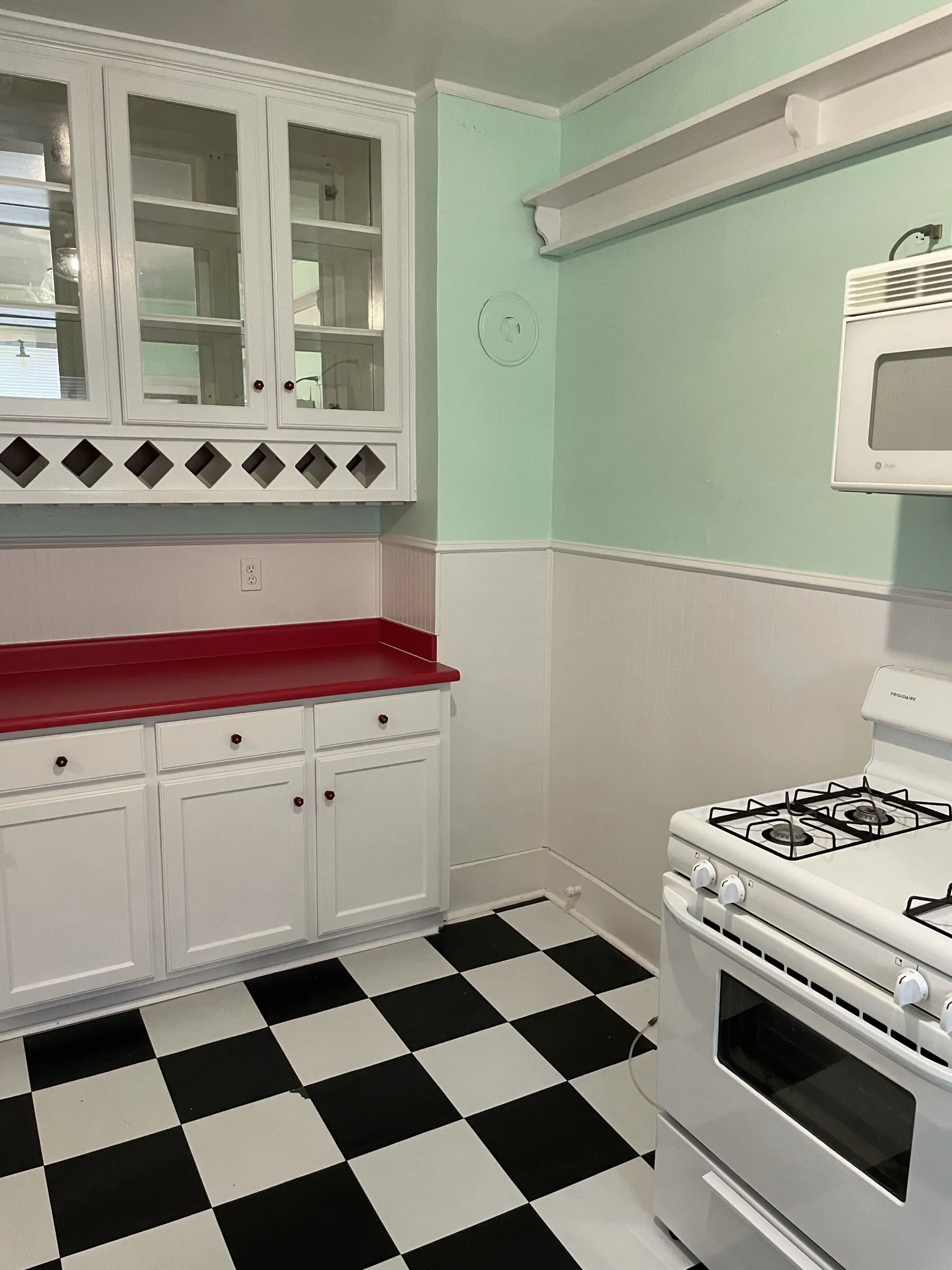 Kitchen featuring white gas range oven, white cabinetry, a wainscoted wall, dark countertops, and dark flooring