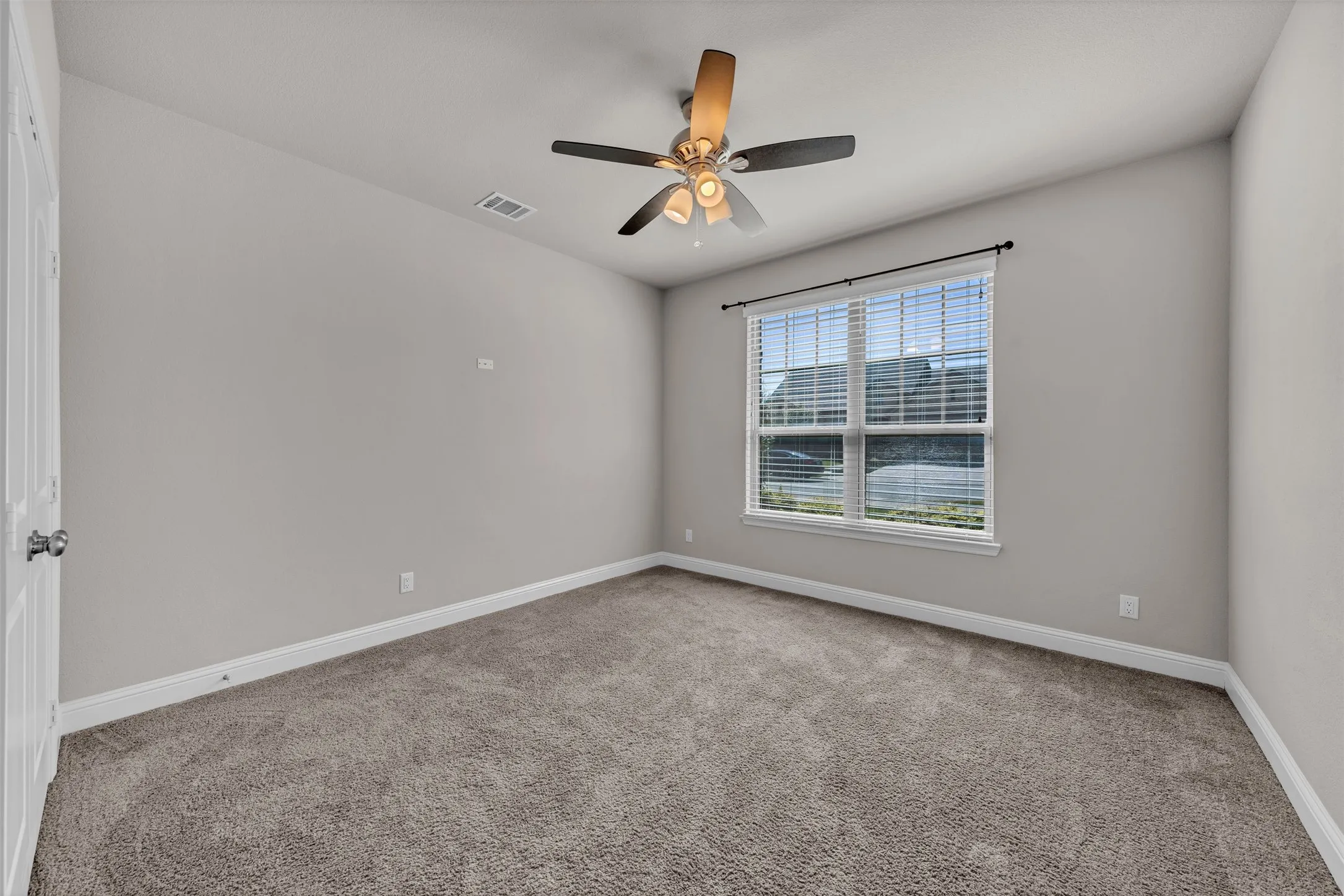 Neutral tone wall paint, carpet flooring, a window with blinds, and a ceiling fan with integrated lighting