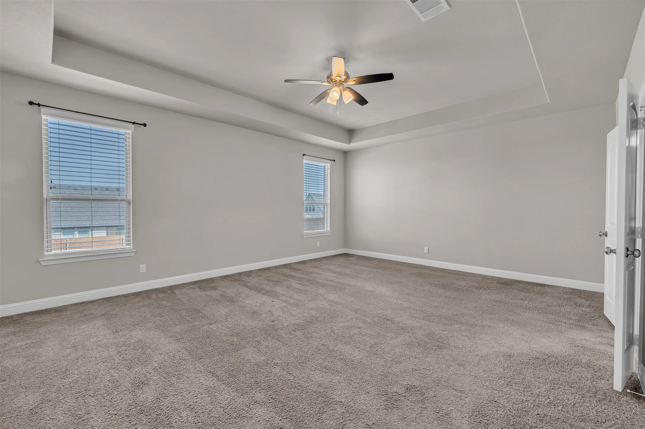 Tray ceiling with a ceiling fan, two windows with blinds, and carpeting