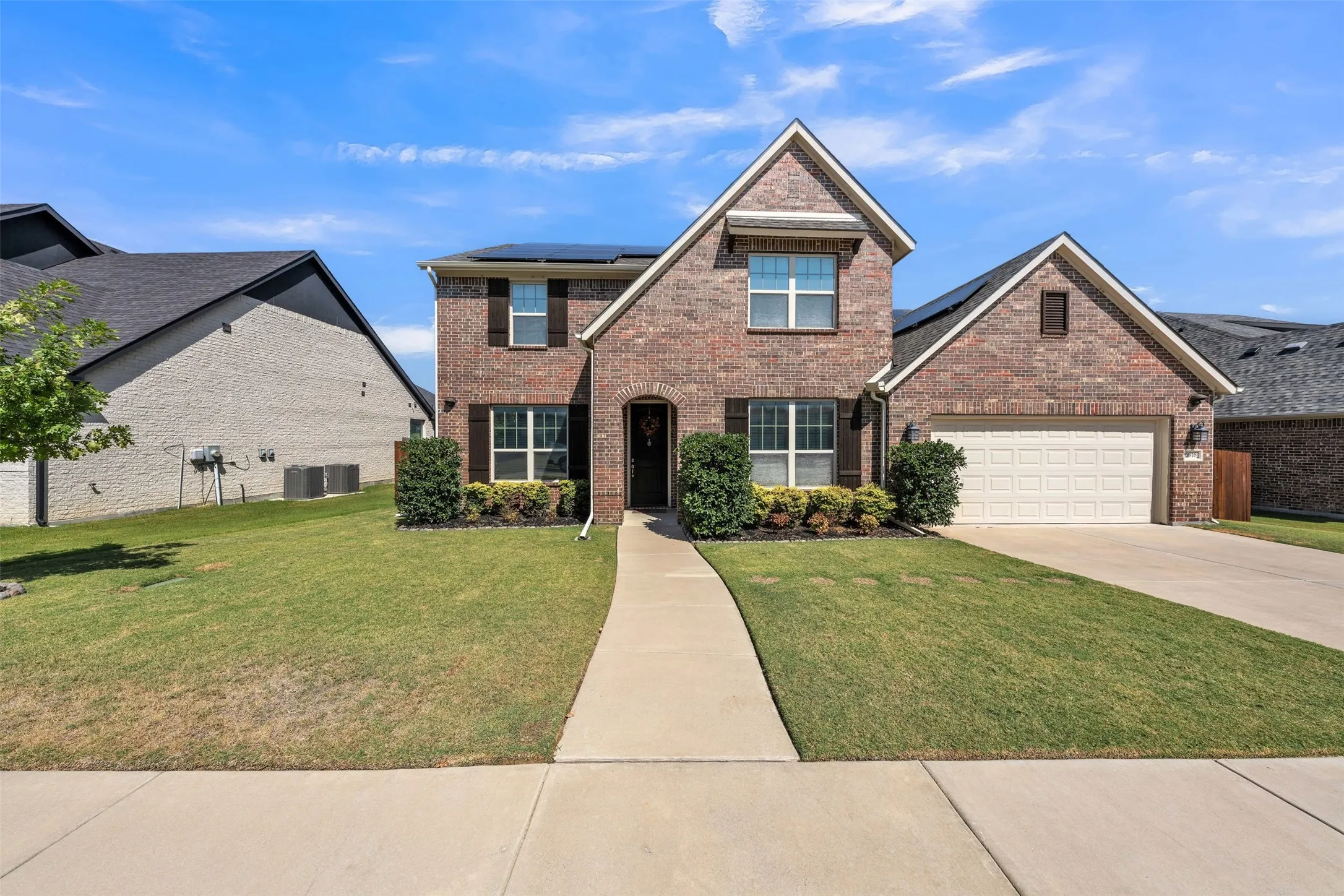 Brick exterior with gabled roof lines, attached two-car garage, concrete driveway, and front walkway