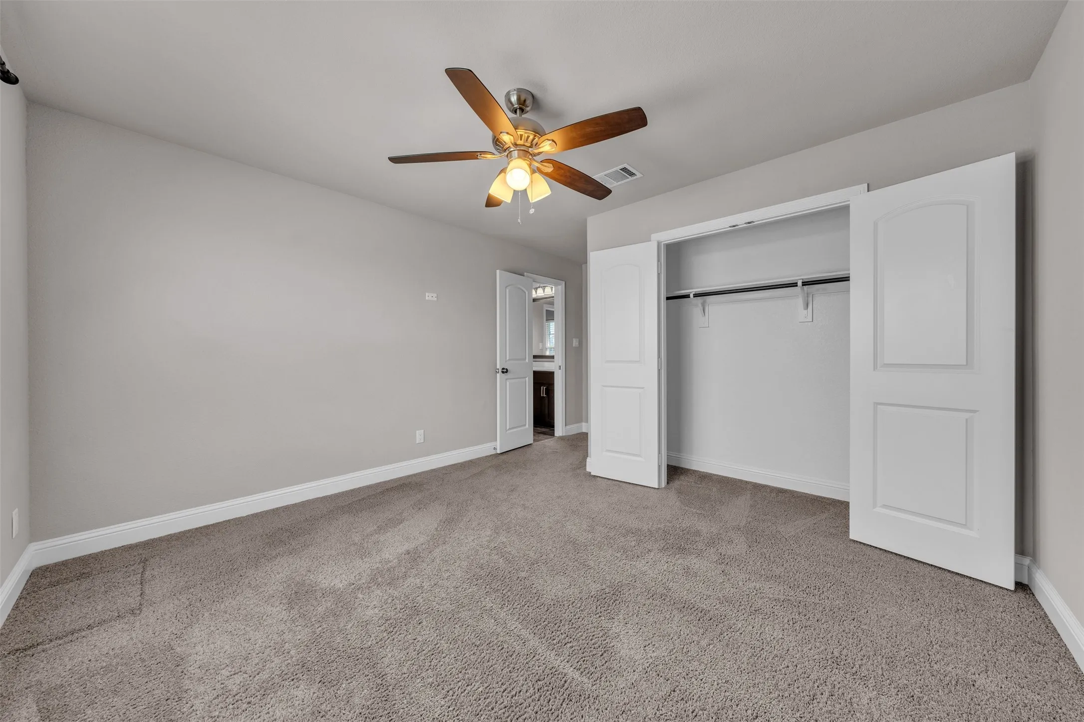 Plush carpeting, neutral wall tones, ceiling fan with light fixture, and a spacious closet with bi-fold doors