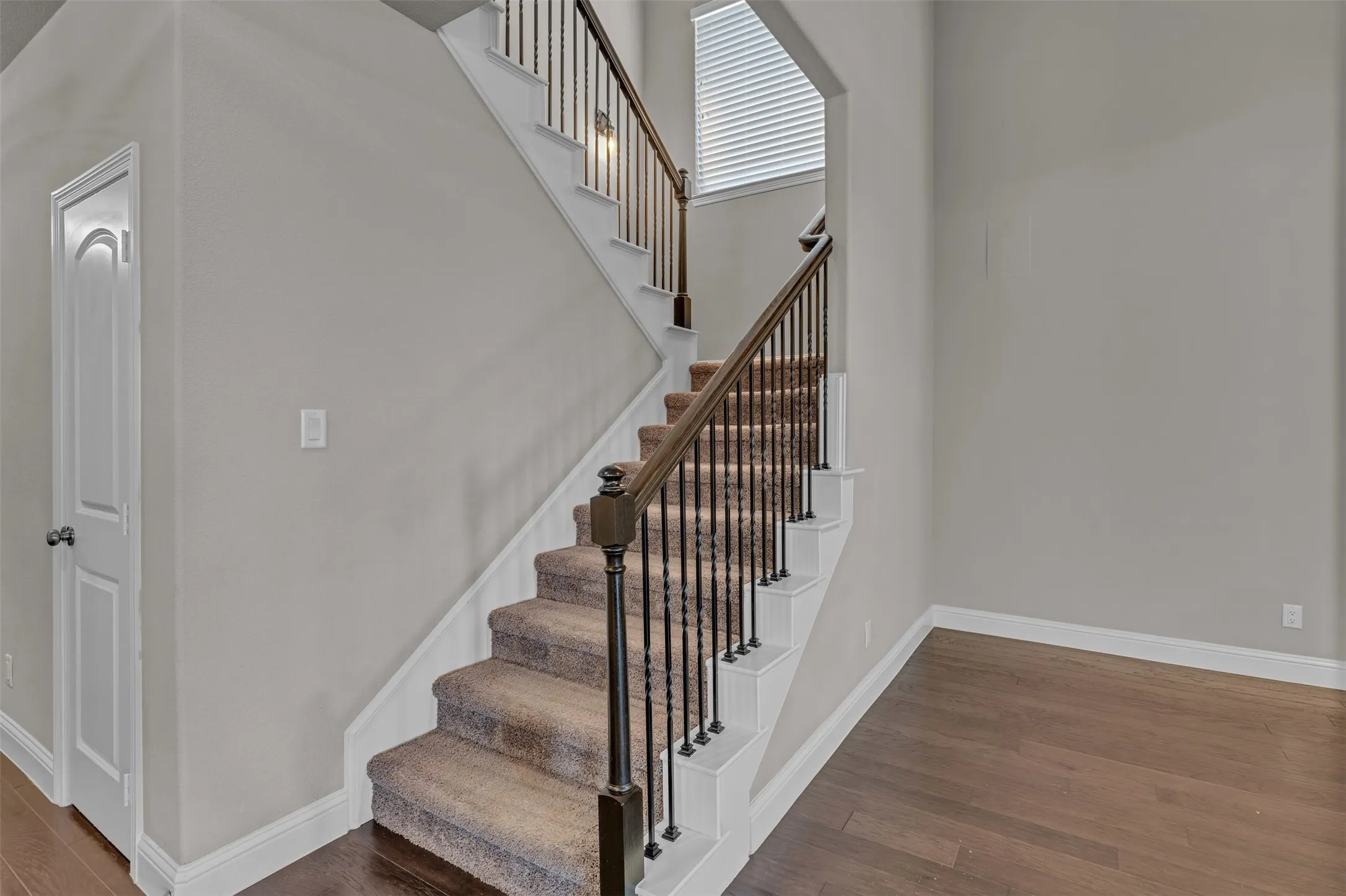 Staircase featuring wood-finish handrails, decorative metal balusters, and carpeted treads