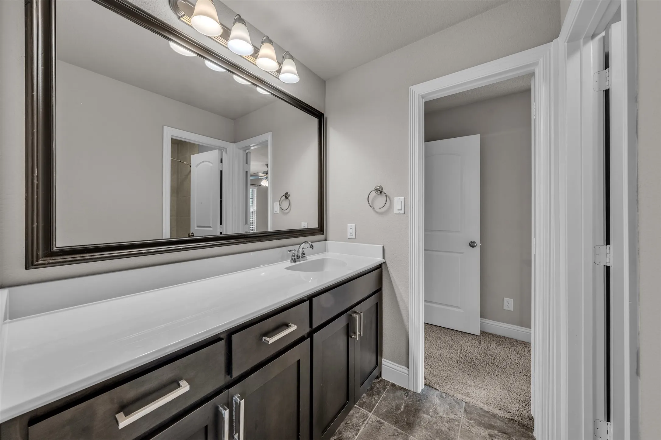 Spacious vanity with a white countertop, dark wood cabinetry, rectangular undermount sink, and a large framed mirror