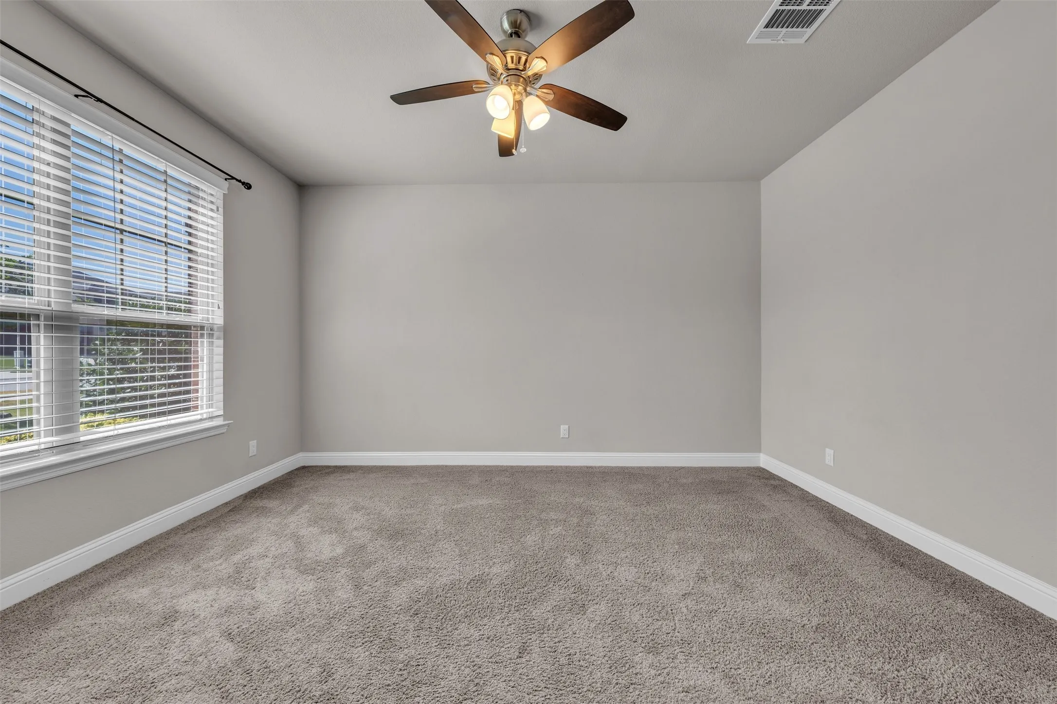 Neutral wall tones, plush carpet flooring, ceiling fan with light fixture, and window with blinds