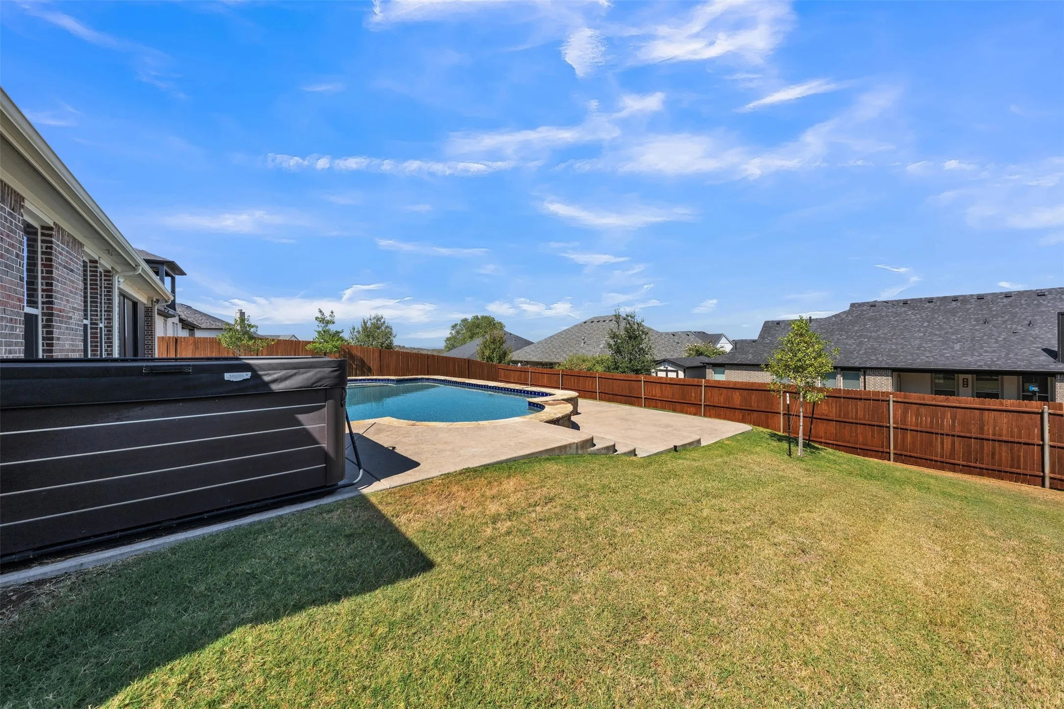 Expansive backyard featuring a built-in swimming pool, integrated hot tub, concrete pool decking, and wood fencing
