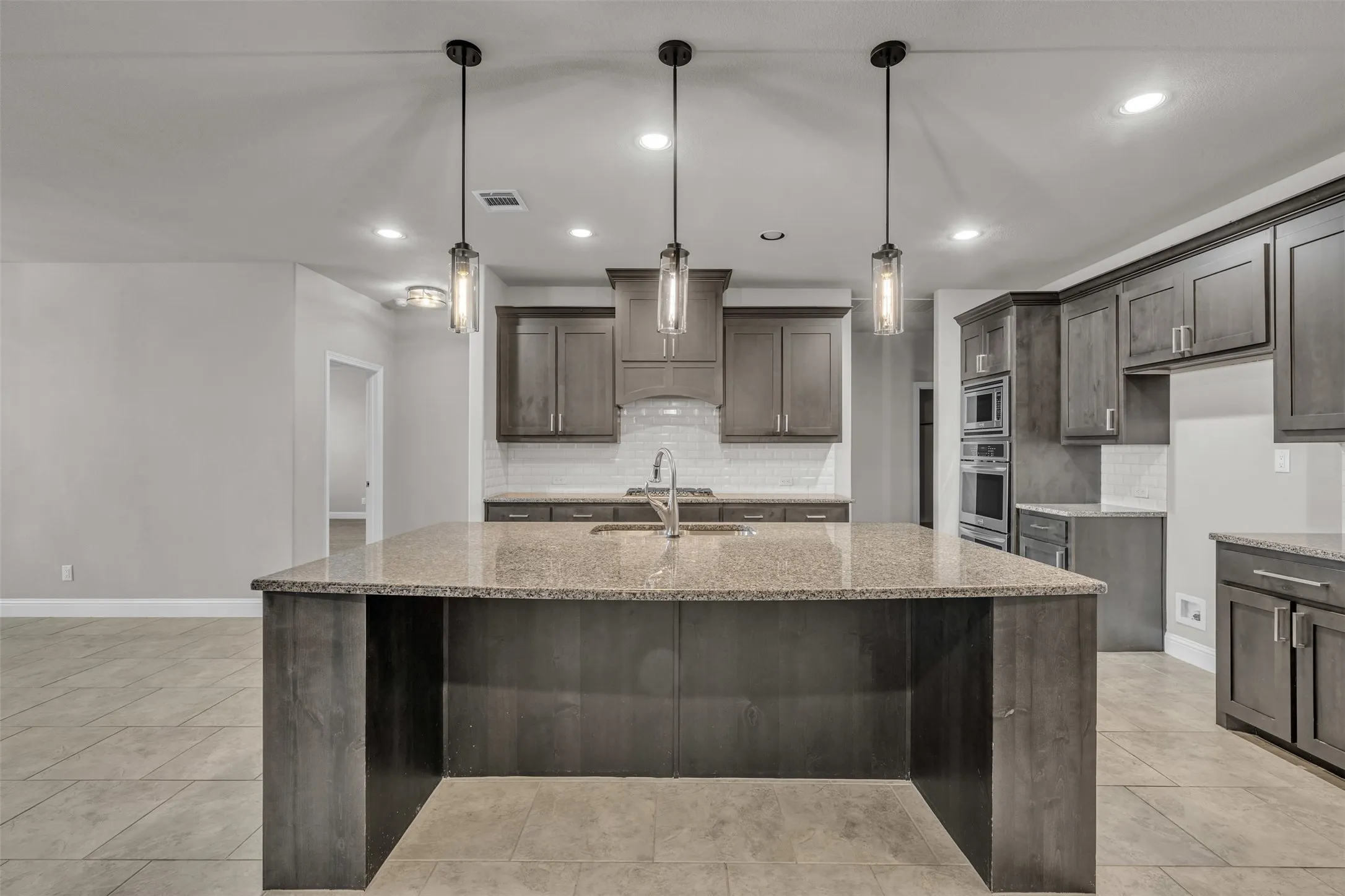 Expansive kitchen island with granite countertop, dark wood-finish cabinetry, stainless steel appliances, and pendant lighting