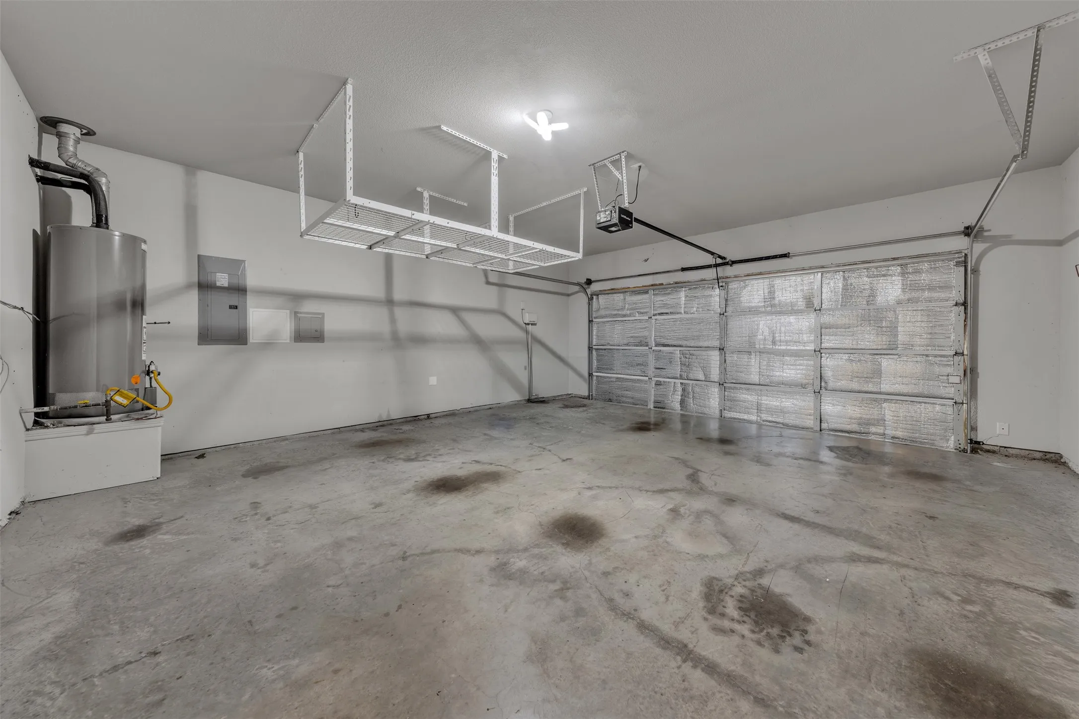 Concrete floor garage with a single vehicle door, overhead storage racks, and a visible water heater