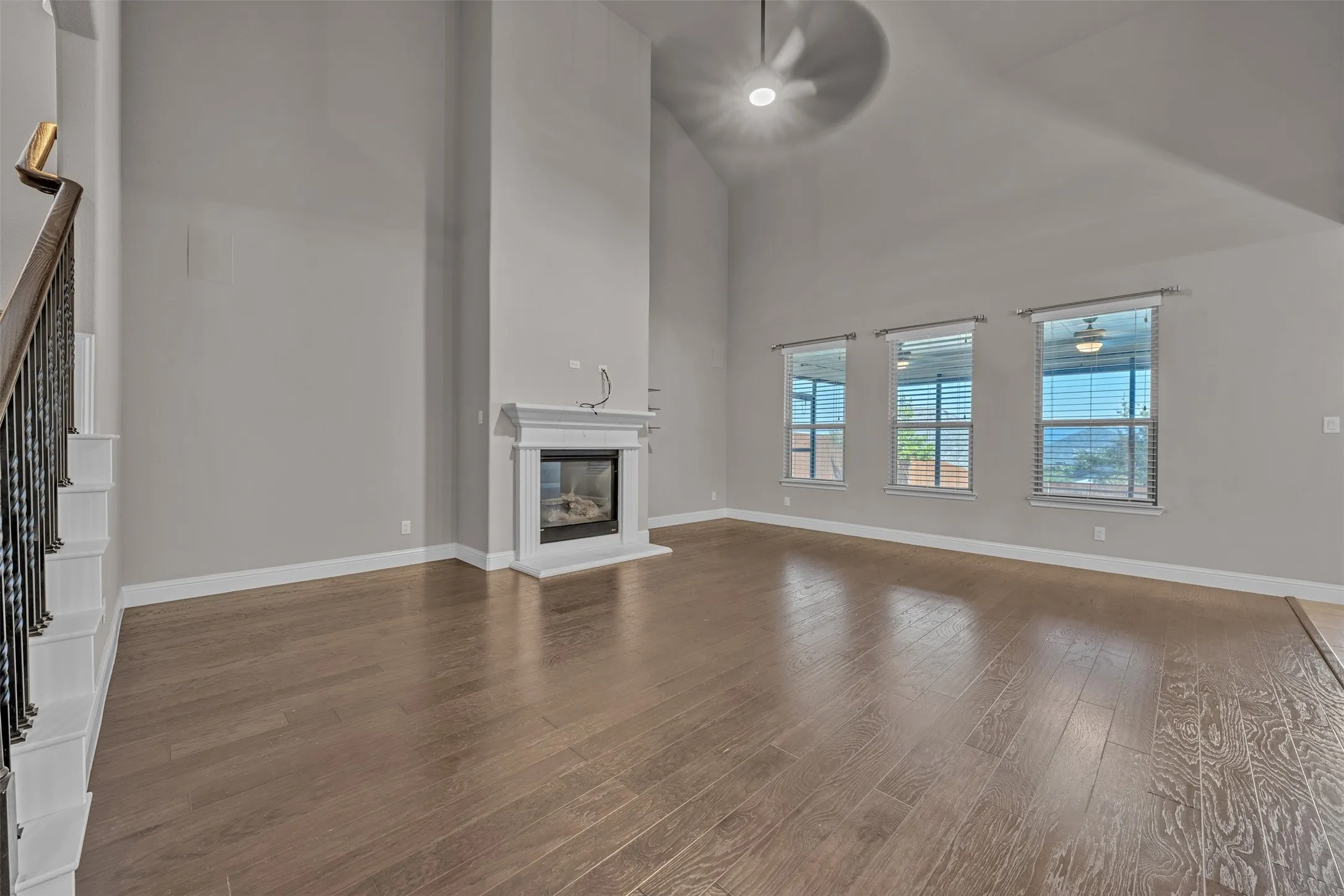 Expansive living space featuring wood-finish flooring, a white mantel fireplace, vaulted ceilings, and a ceiling fan with integrated lighting