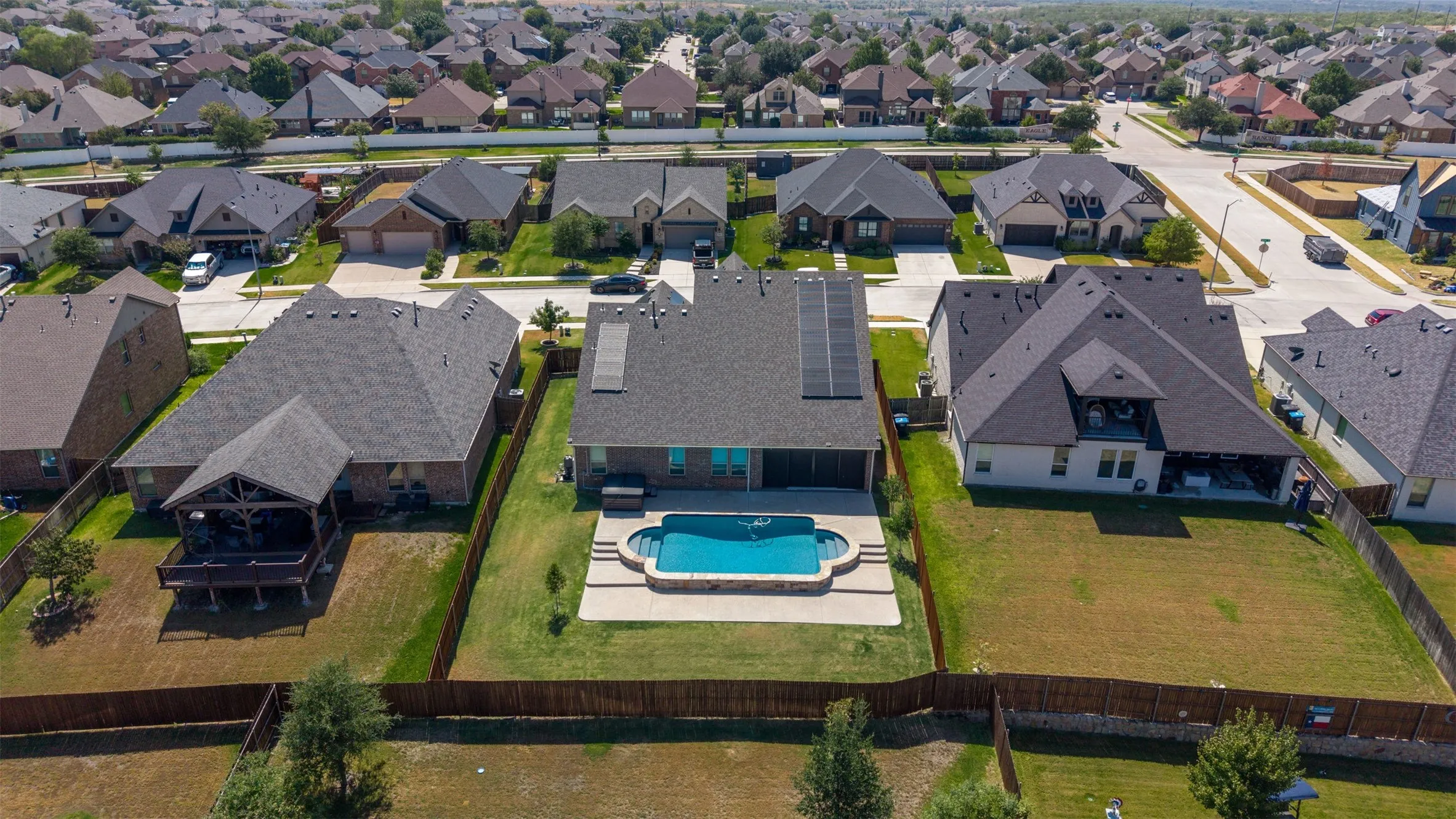 Fenced backyard featuring an in-ground swimming pool with stone coping, concrete patio, and mature landscaping