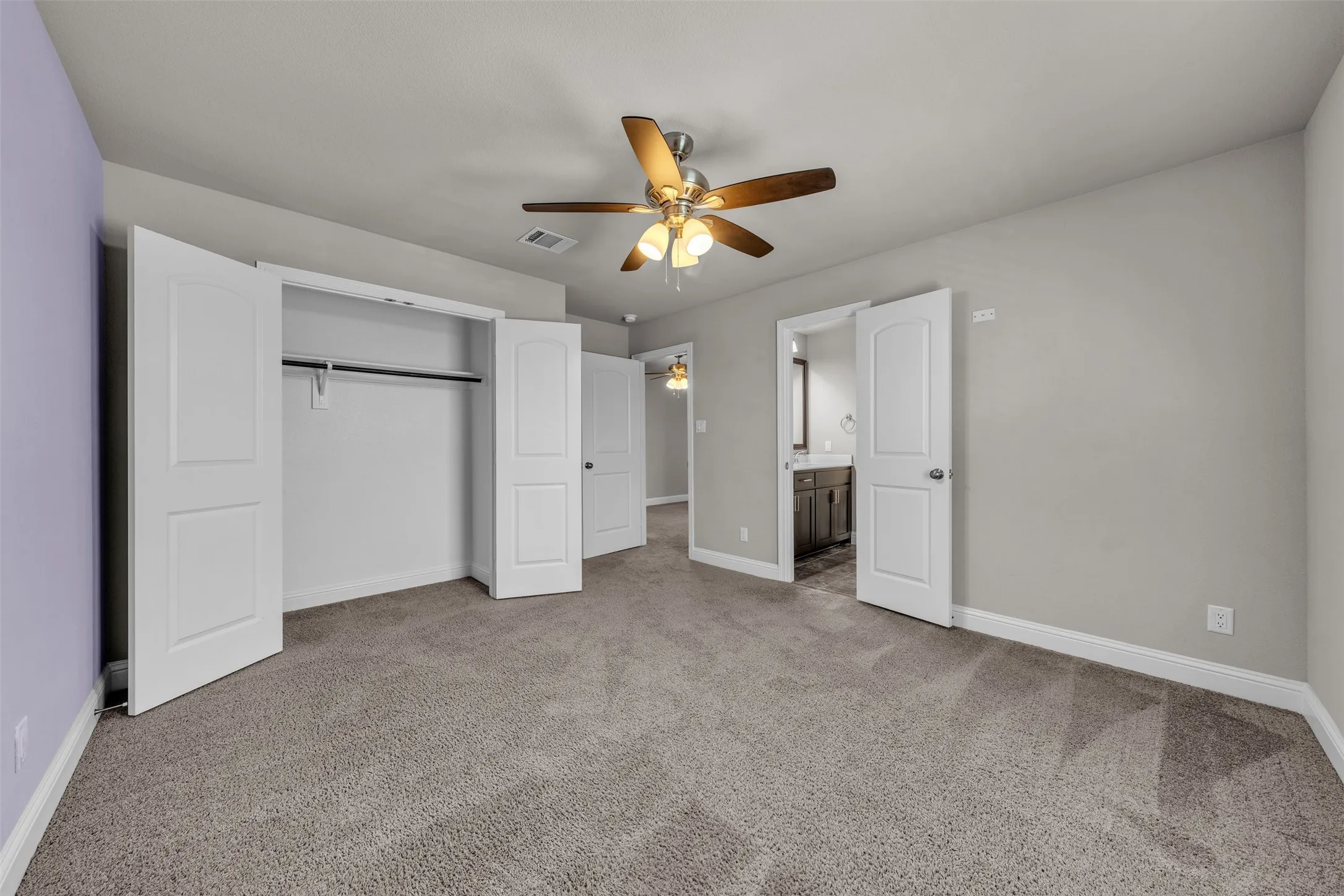 Spacious room with plush carpet flooring, a ceiling fan, and ample closet space