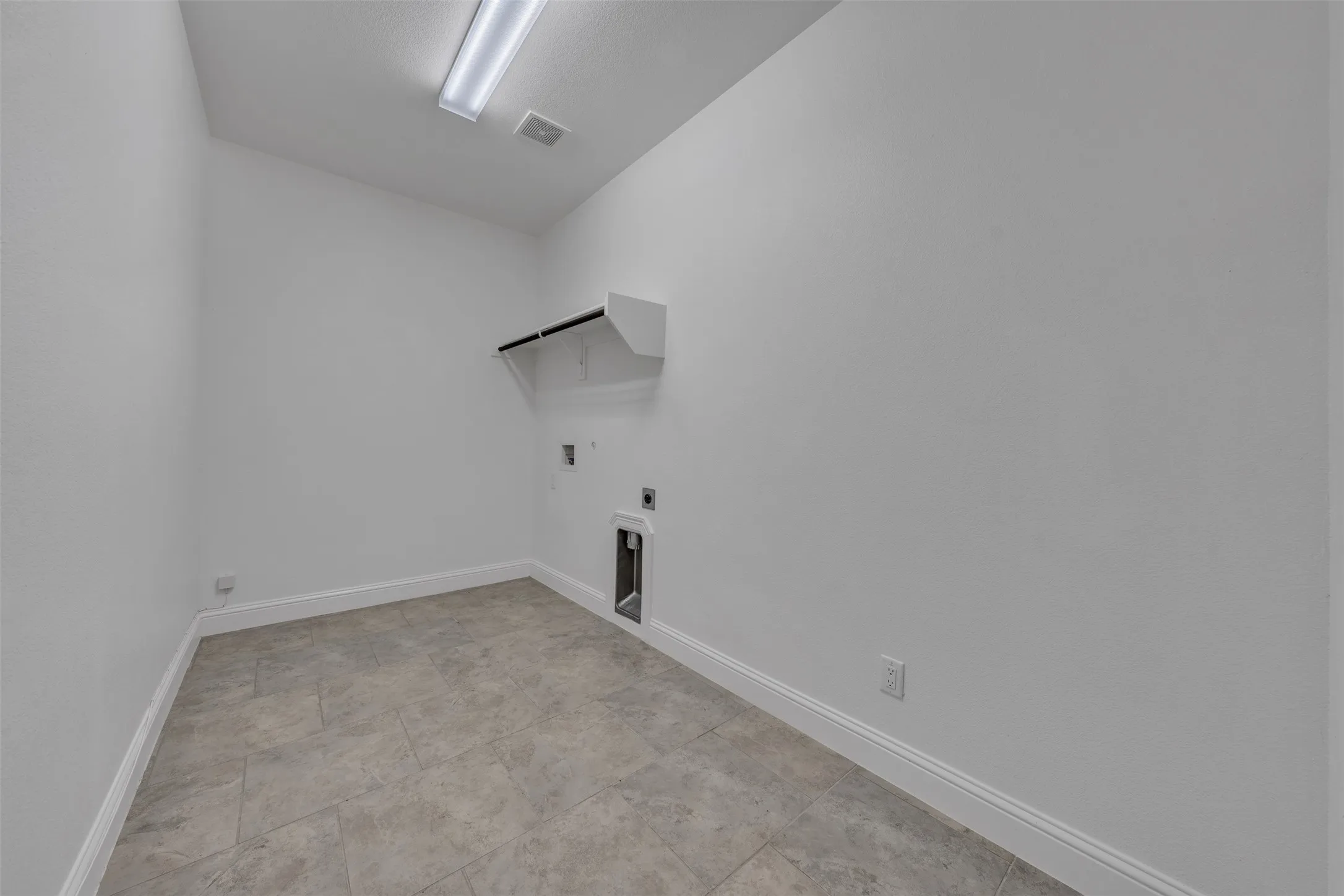 White walls with tile flooring, featuring a built-in shelf with hanging rod and laundry hookups