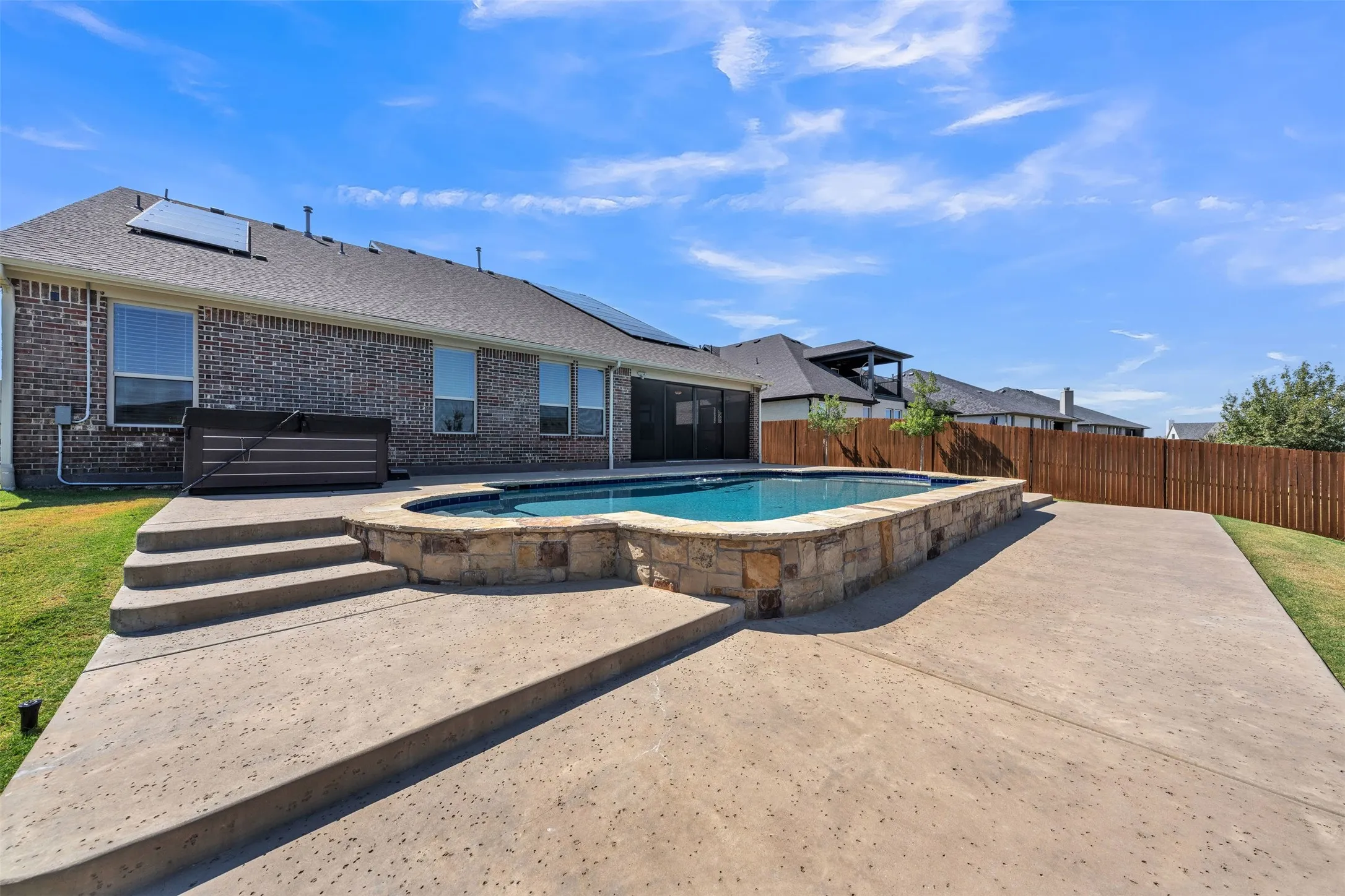 Private backyard featuring a swimming pool with stone surround, concrete patio, and slatted wood fencing