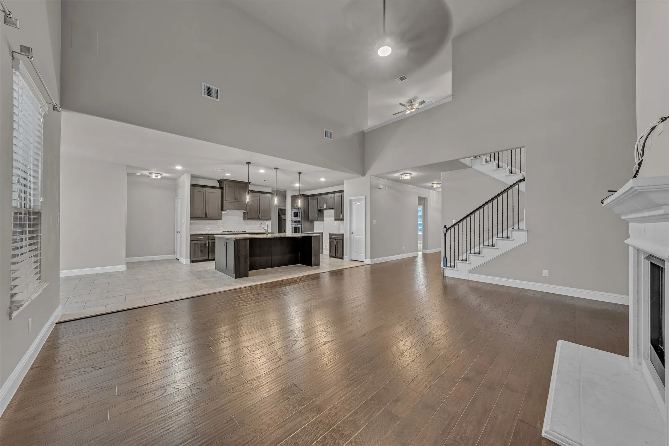 Two-story great room with wood-finish flooring, a white mantel fireplace, and staircase with wrought iron balusters