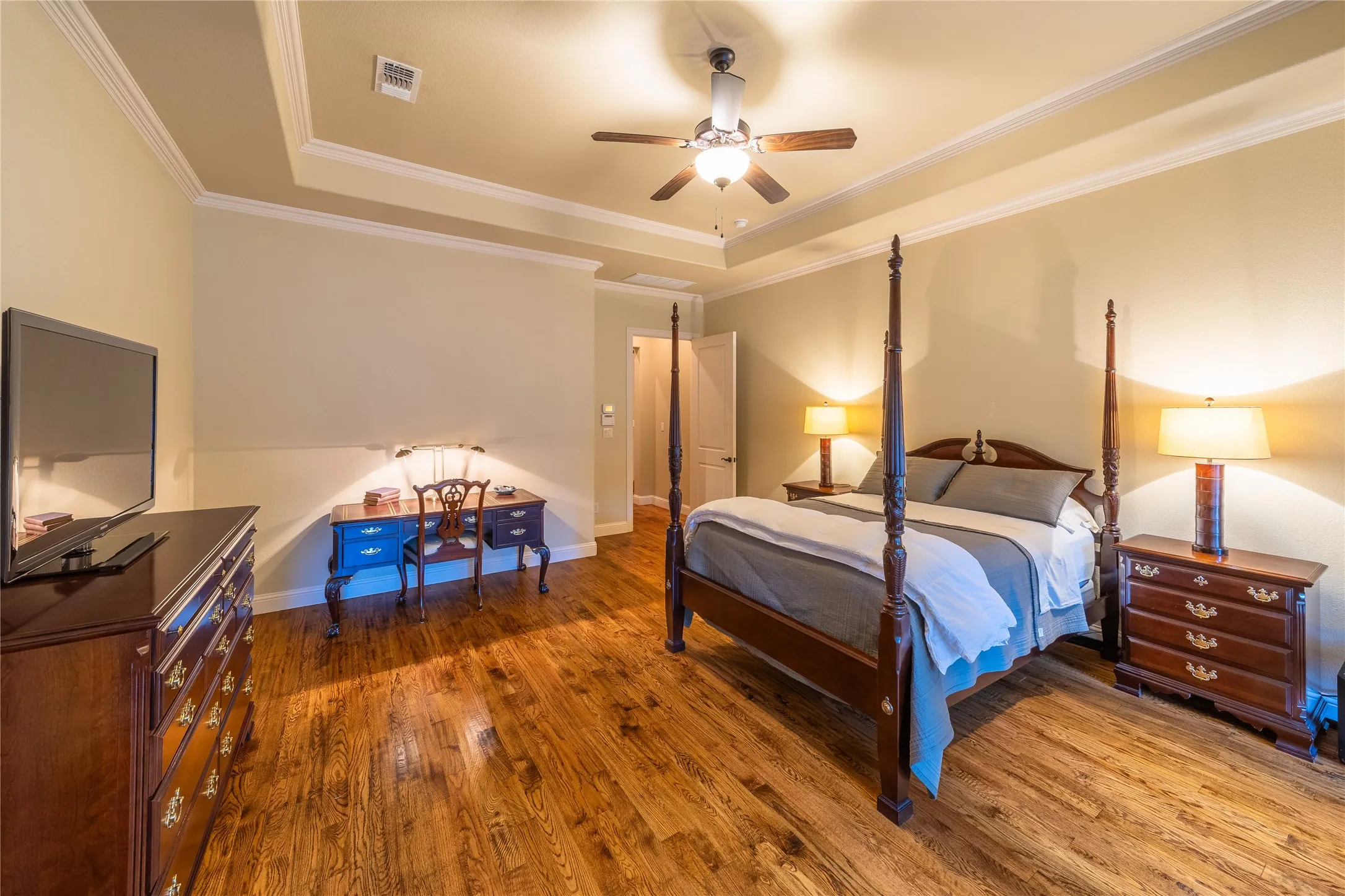 The primary bedroom is located at the back of the home. The room features coffered ceilings. The door in the center of the photo leads to the hallway which connects to the mudroom and the living room.
