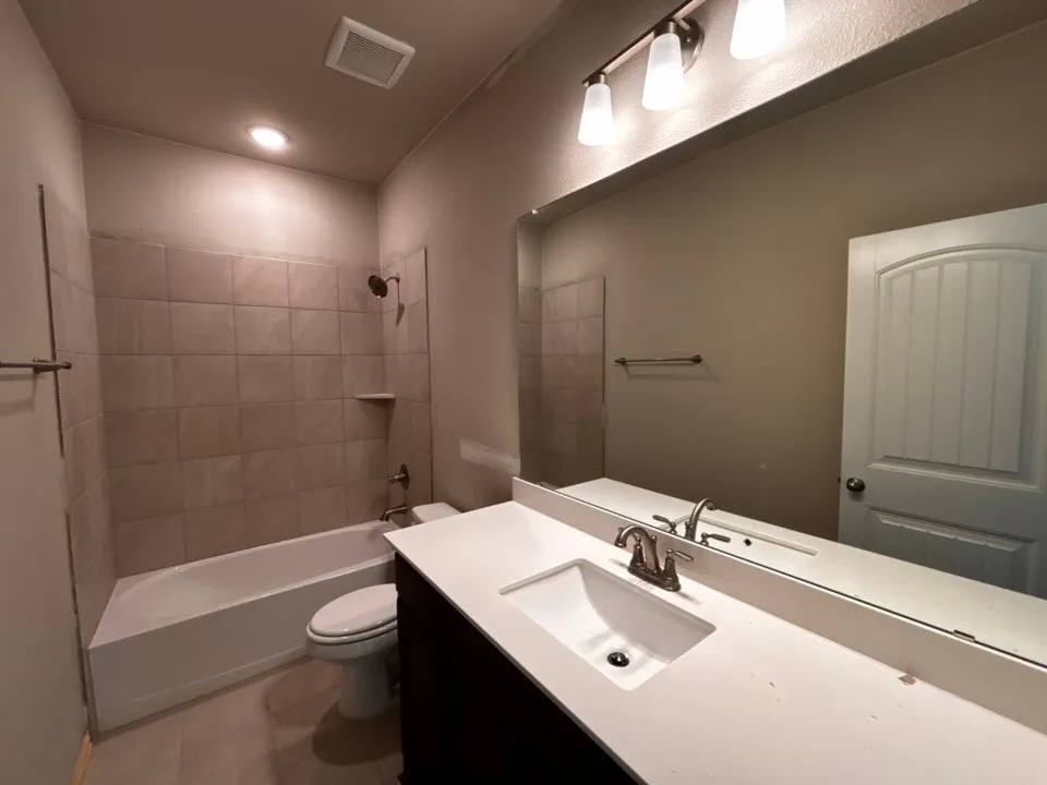 Full-length vanity mirror, sleek white countertop with integrated sink, dark wood-finish cabinetry, tiled shower surround, and a tub with shower combination