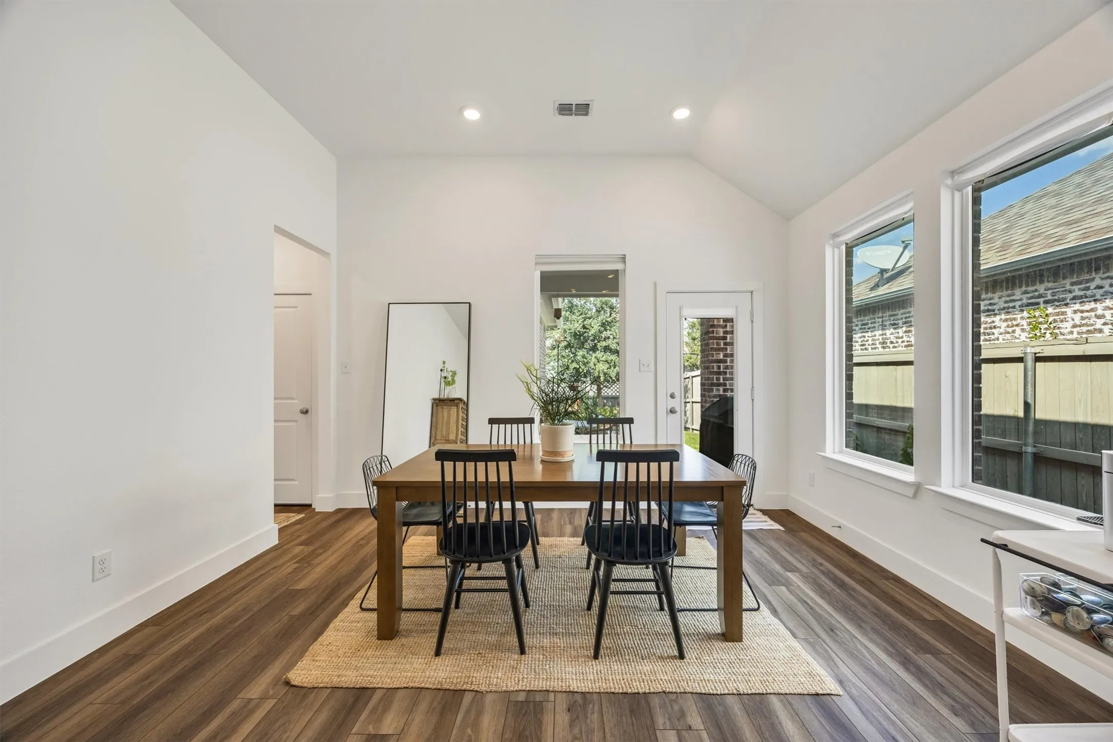 Vaulted ceiling with recessed lighting, wood-finish flooring, multiple windows, and a glass-paneled exterior door