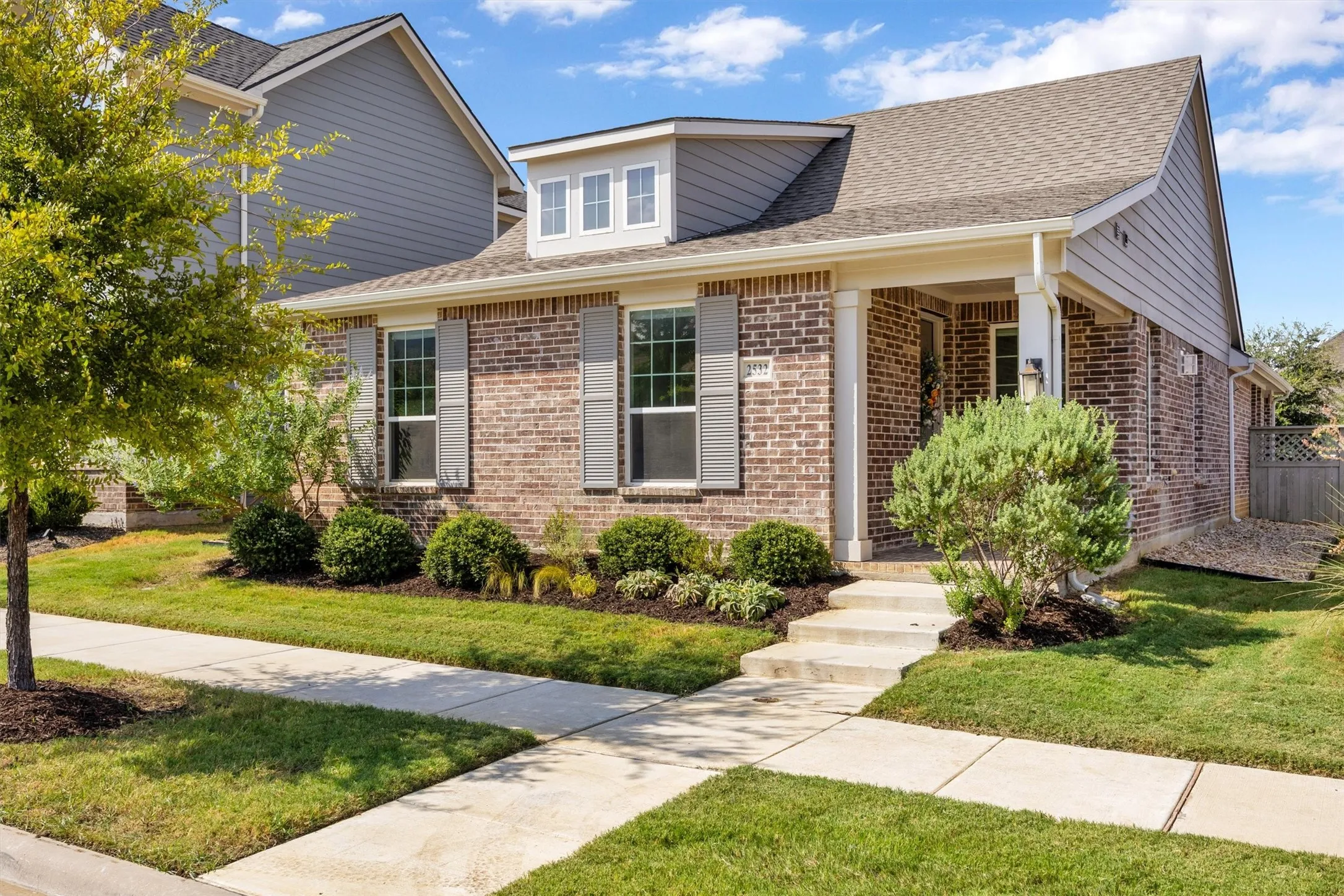 Brick exterior with siding accents, covered front porch, concrete steps, and landscaped front yard with mature plantings