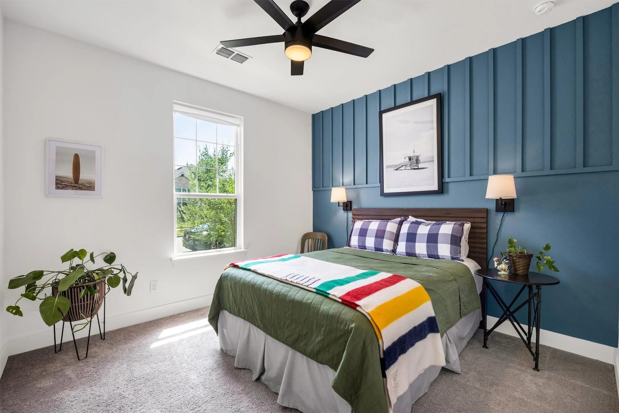 Window with natural light, textured accent wall, wood-finish headboard, wall-mounted sconce lighting, and ceiling fan with integrated light