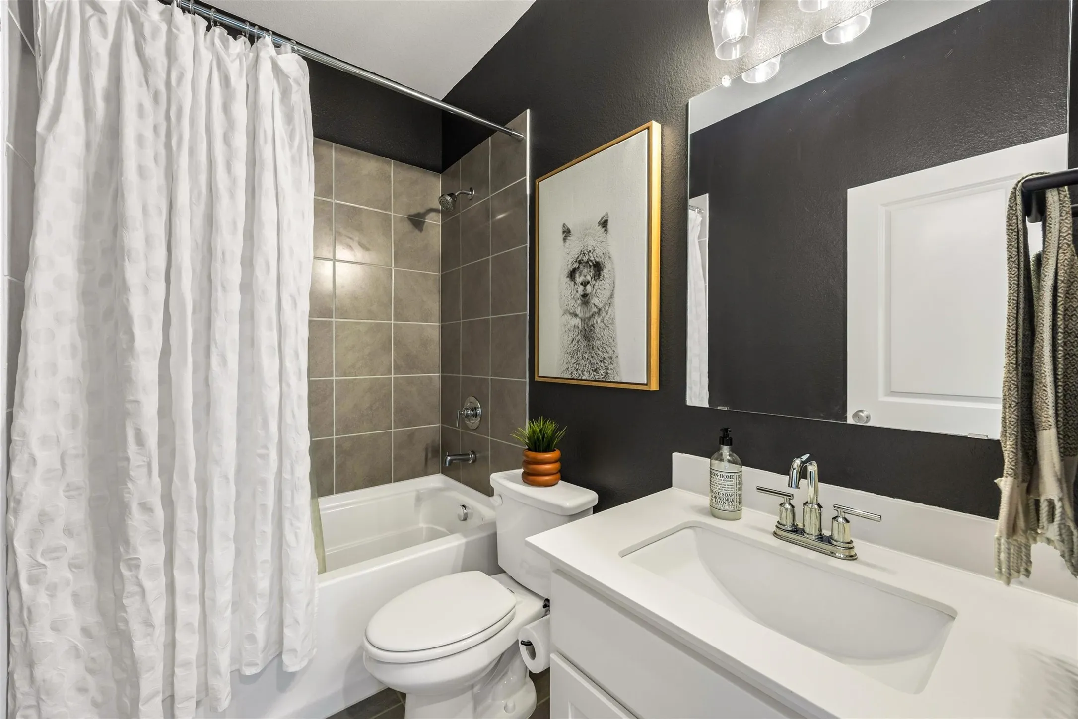 Integrated bathtub and shower with brown tile surround, white vanity with an undermount sink, and brushed nickel fixtures