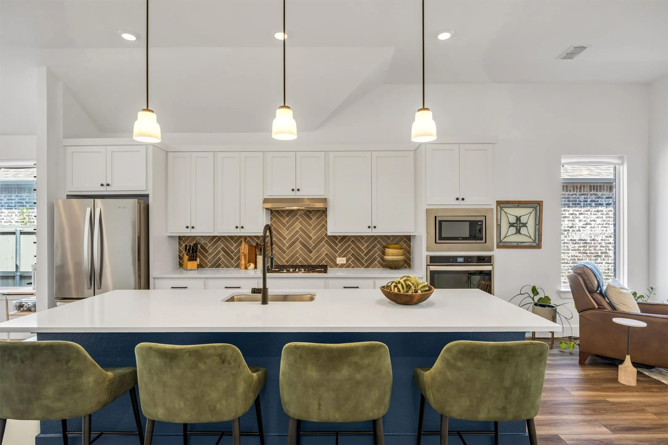 Kitchen featuring a large island with seating, white shaker-style cabinetry, stainless steel appliances, a herringbone tile backsplash, and recessed lighting