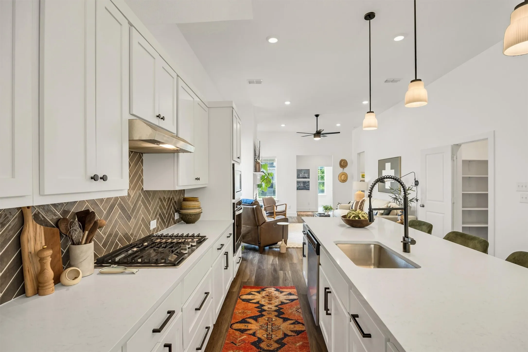 Open-concept kitchen featuring white cabinetry, a gas range with a herringbone tile backsplash, an island with a stainless steel sink, and wood-finish flooring