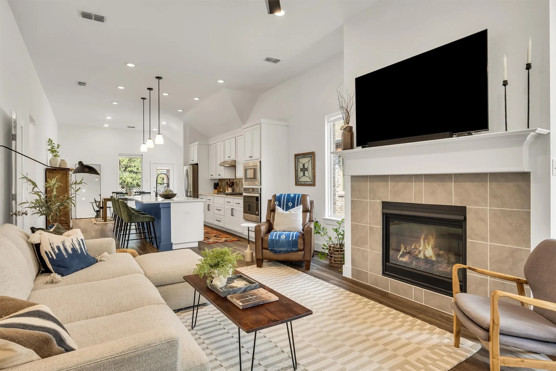 Vaulted ceiling, recessed lighting, tile-surround fireplace, wood-finish flooring, and a kitchen island with pendant lighting