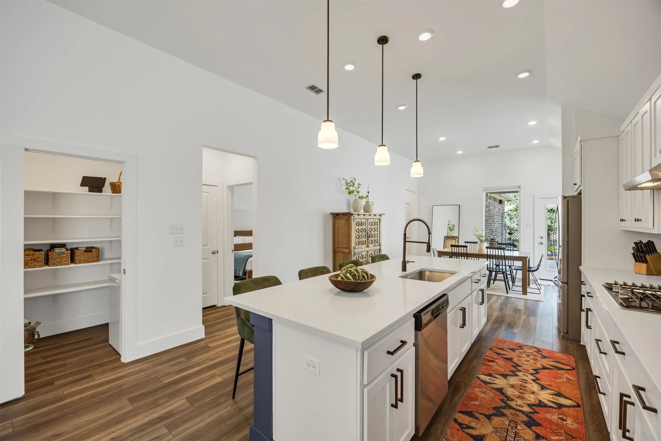 Kitchen featuring a gas range, stainless steel appliances, a center island with a sink, pendant lighting, and wood-finish flooring