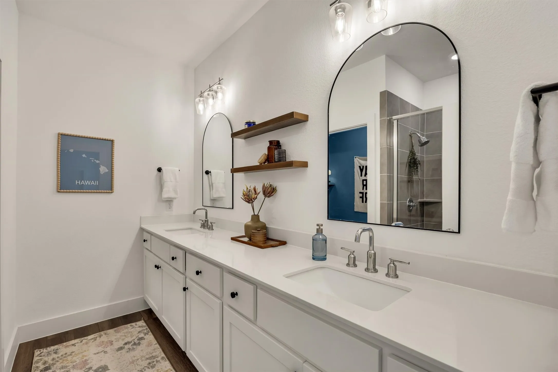 Double vanity with integrated sinks, white cabinetry with black hardware, and two arched mirrors