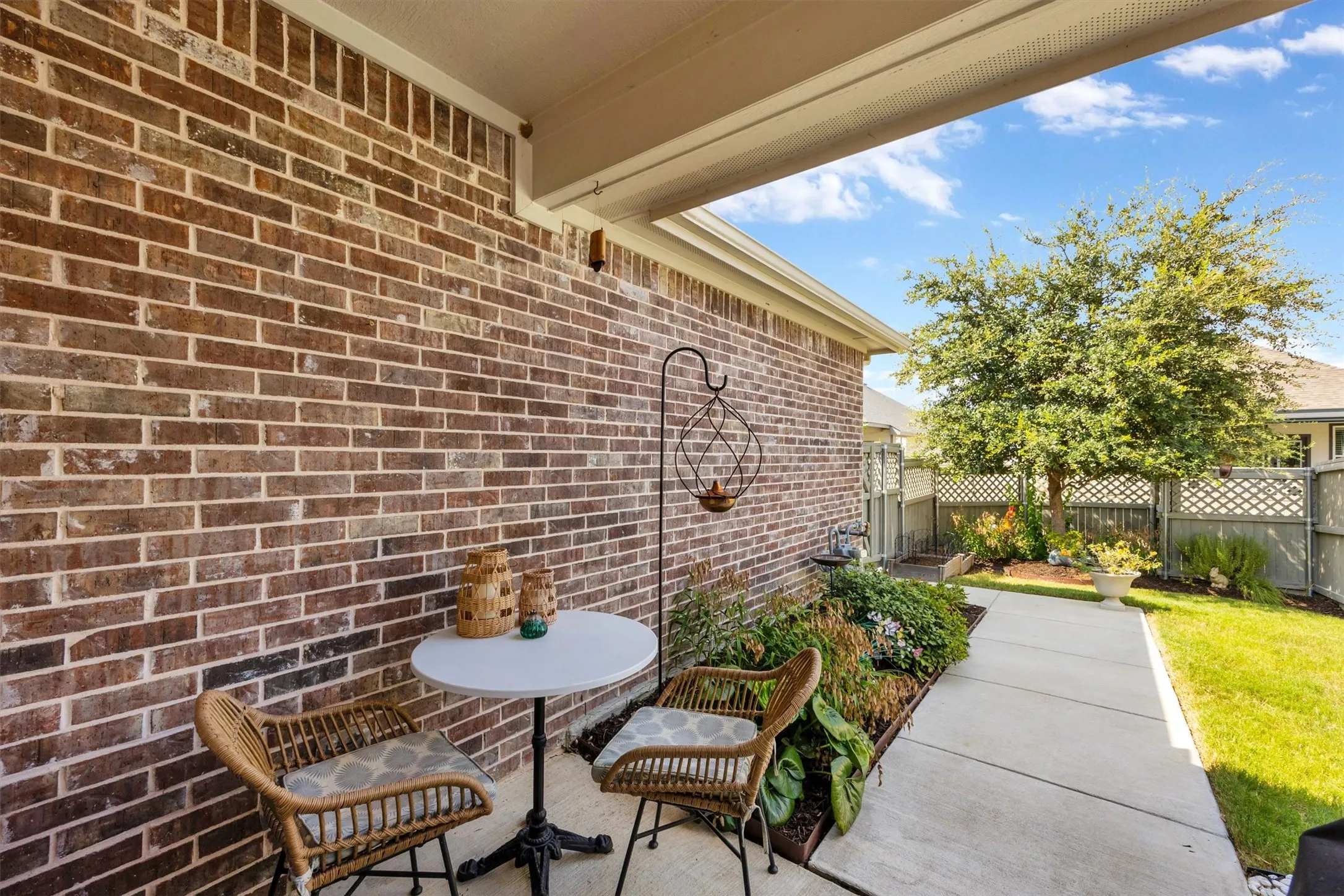Brick exterior wall with a covered patio, concrete pathway, and landscaped garden bed