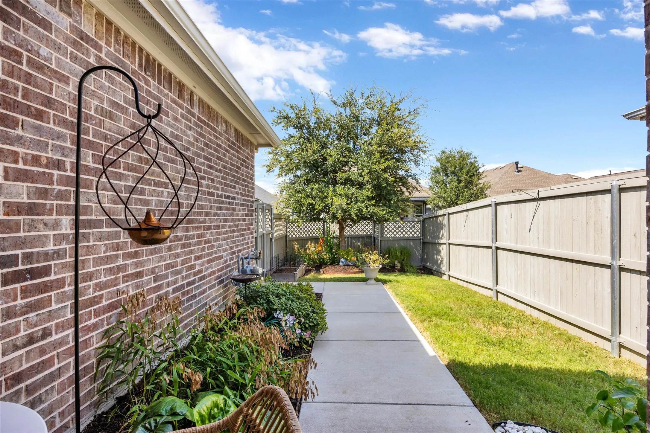 Brick exterior with a concrete walkway, manicured lawn, and wood privacy fencing