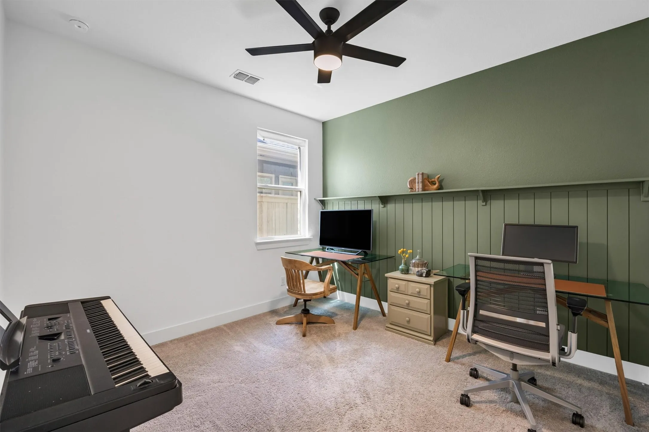 Carpeted room featuring a ceiling fan, a window, and a green accent wall with wainscoting and a built-in shelf
